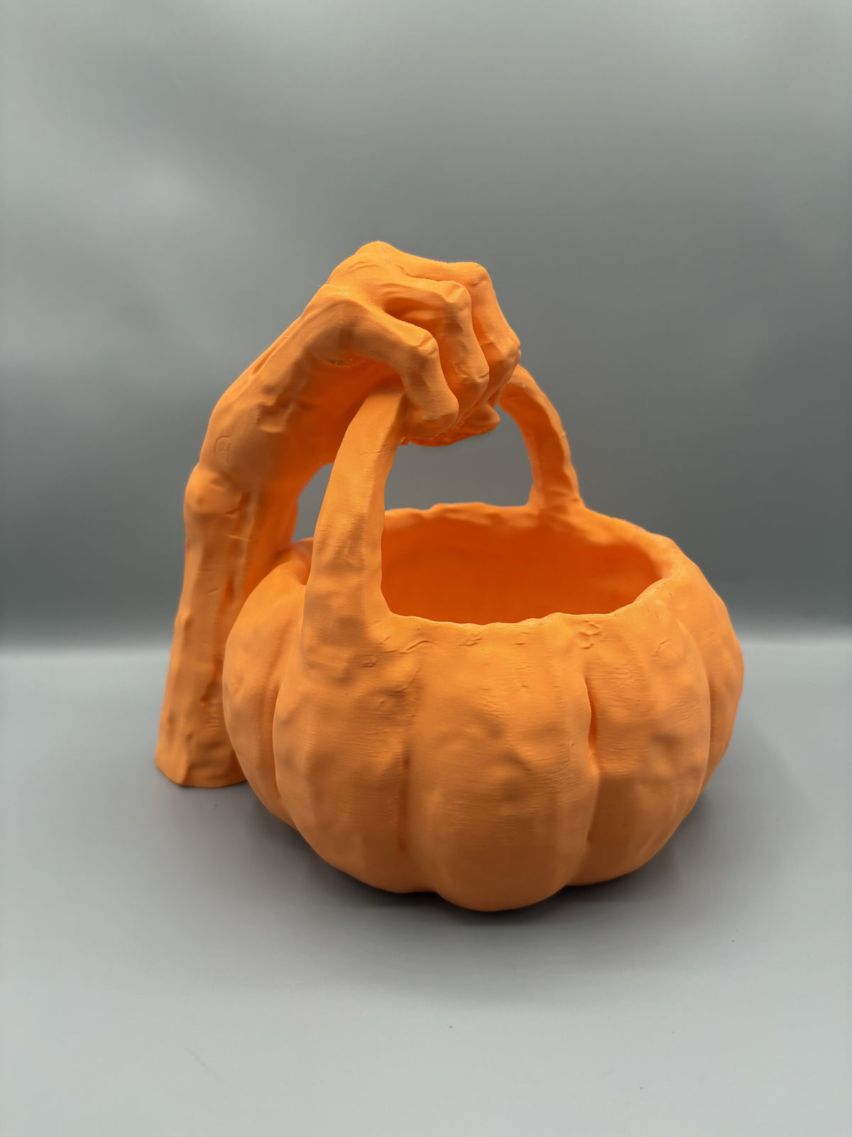 Orange monster hand pumpkin candy bowl, studio front view on a gray background