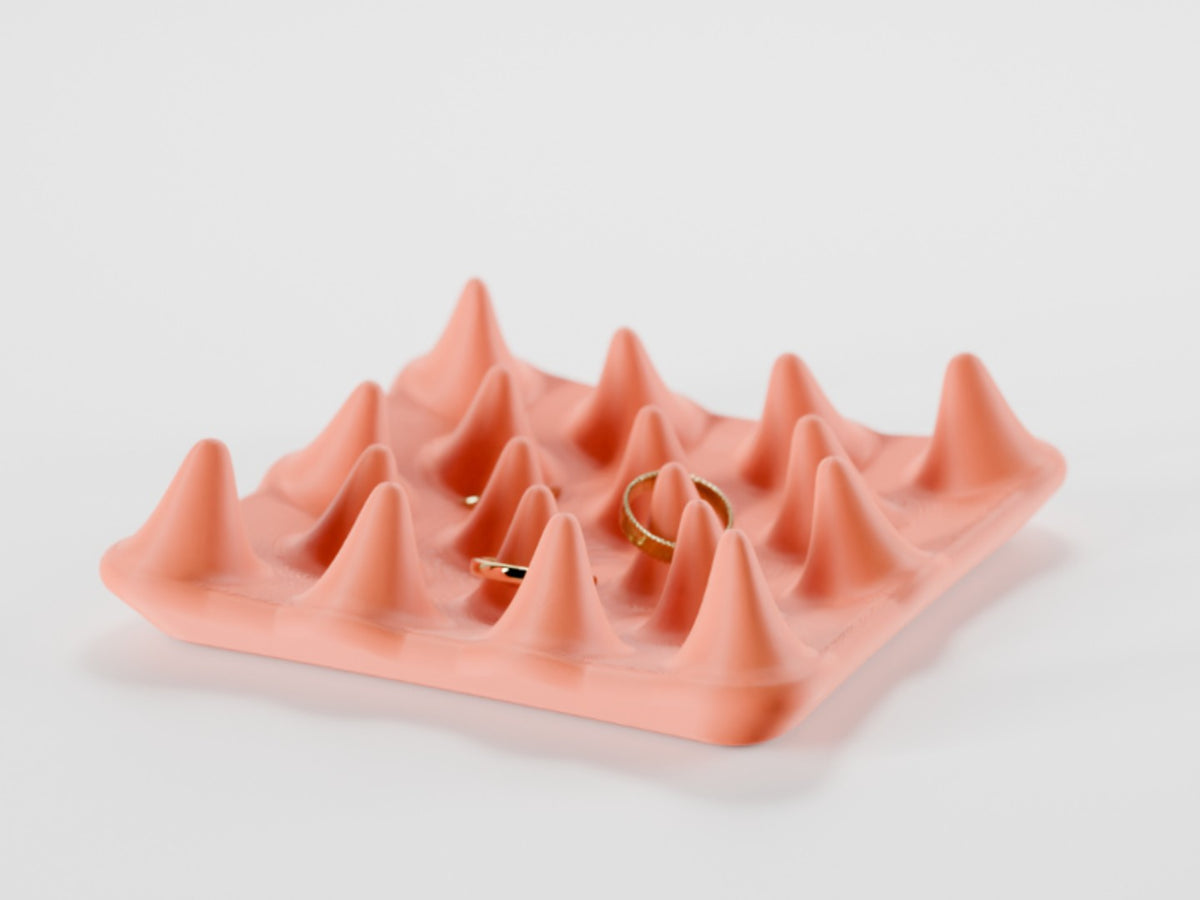 Peach spiked jewelry ring tray with gold rings resting between the peaks