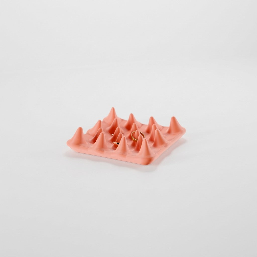 Spiked jewelry ring tray on a white surface with two gold rings on the peaks