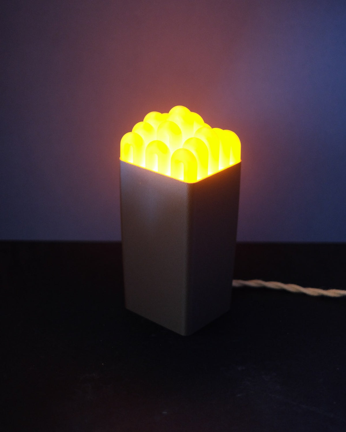 Funky wibble cap table lamp glowing yellow on a soft pink base